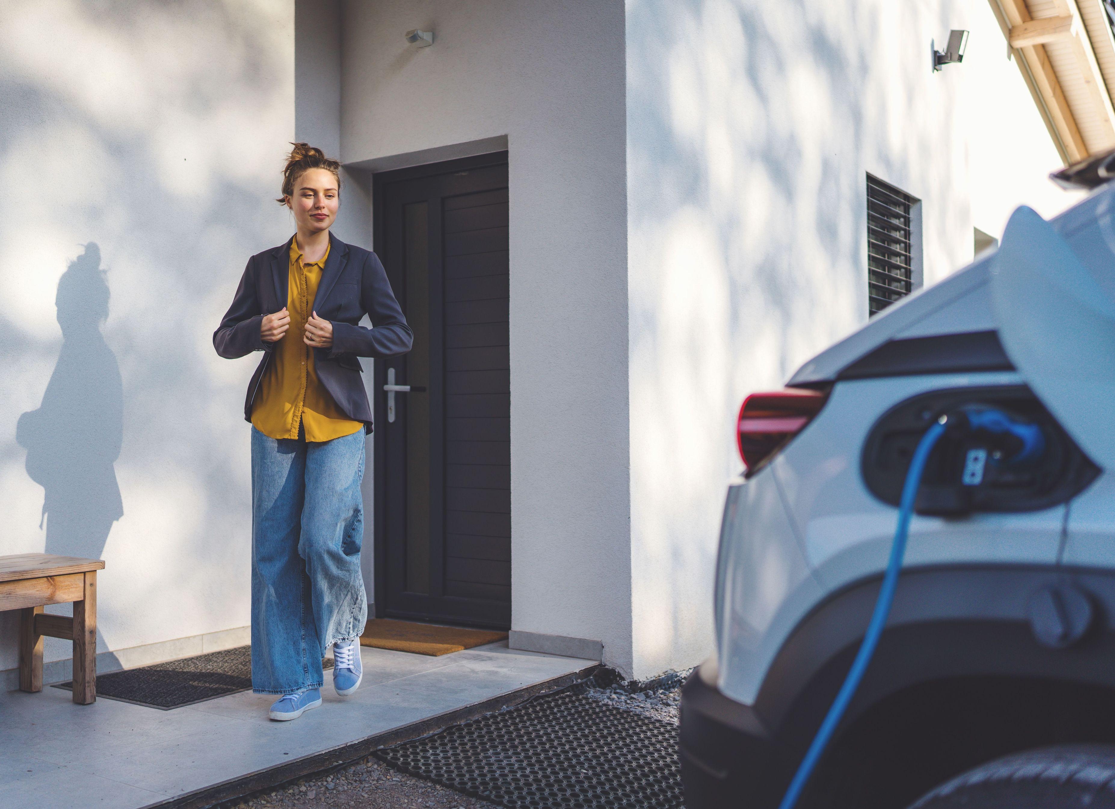 Frau geht von der Haustür zum ladenden E-Auto