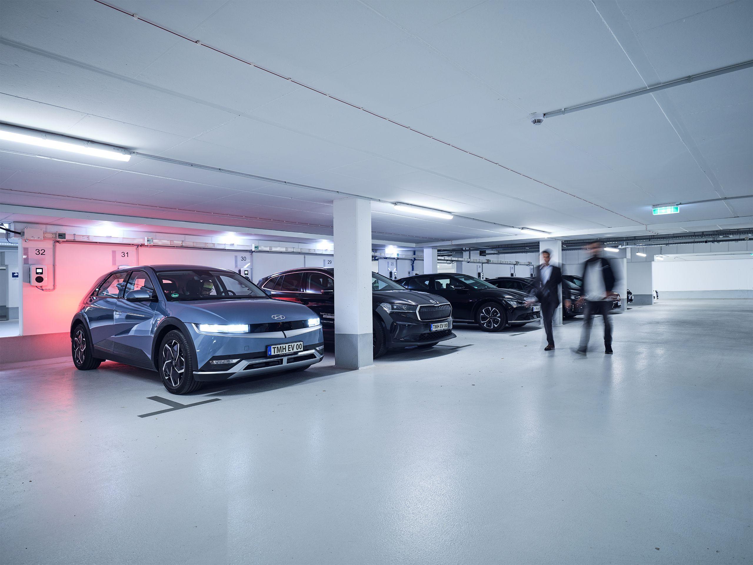 Kollegen laufen durch die Tiefgarage mit ladenden Elektroautos im Hintergrund