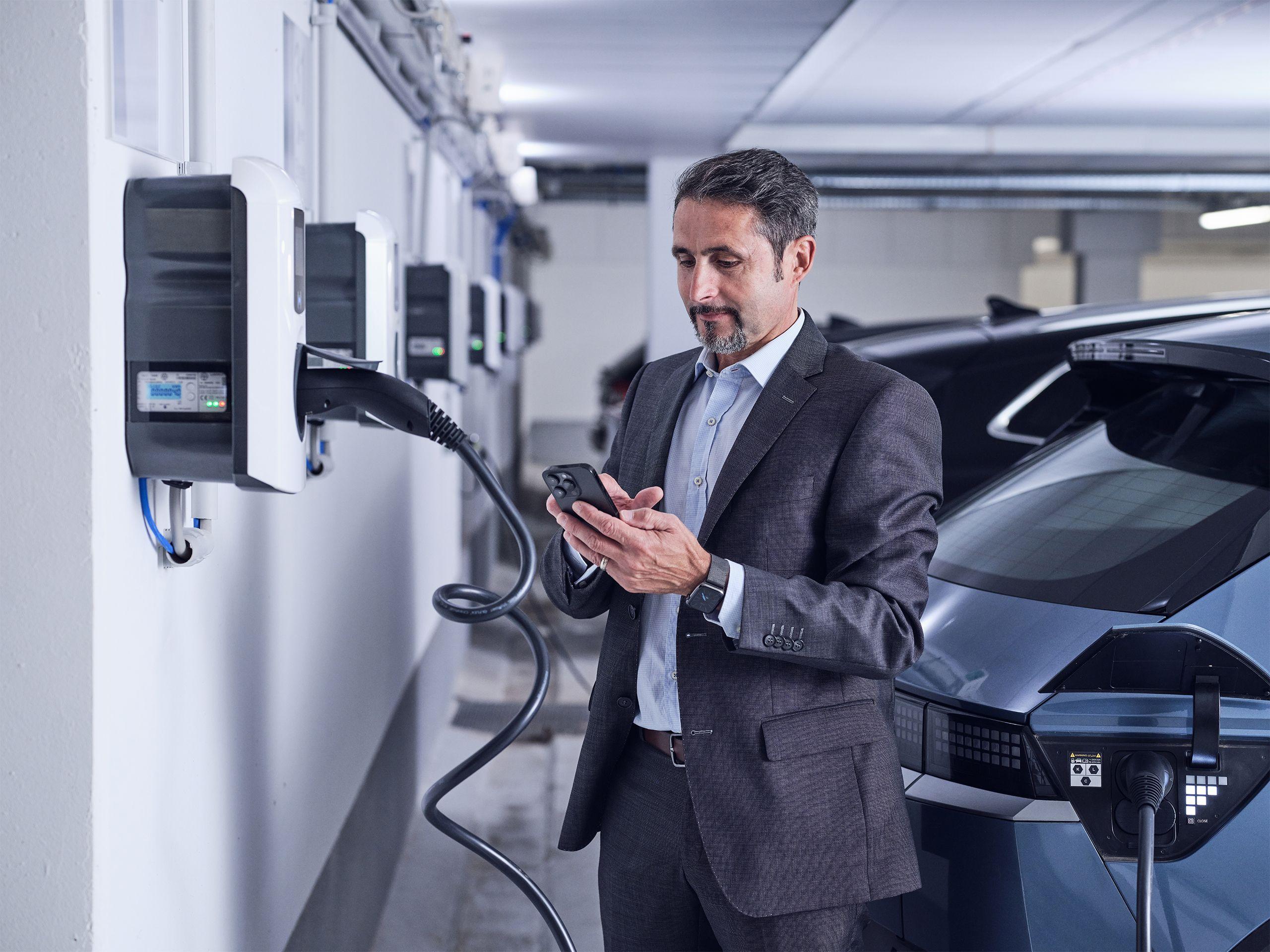 Mann steht mit seinem Handy zur Ladestation gerichtet in der Tiefgarage