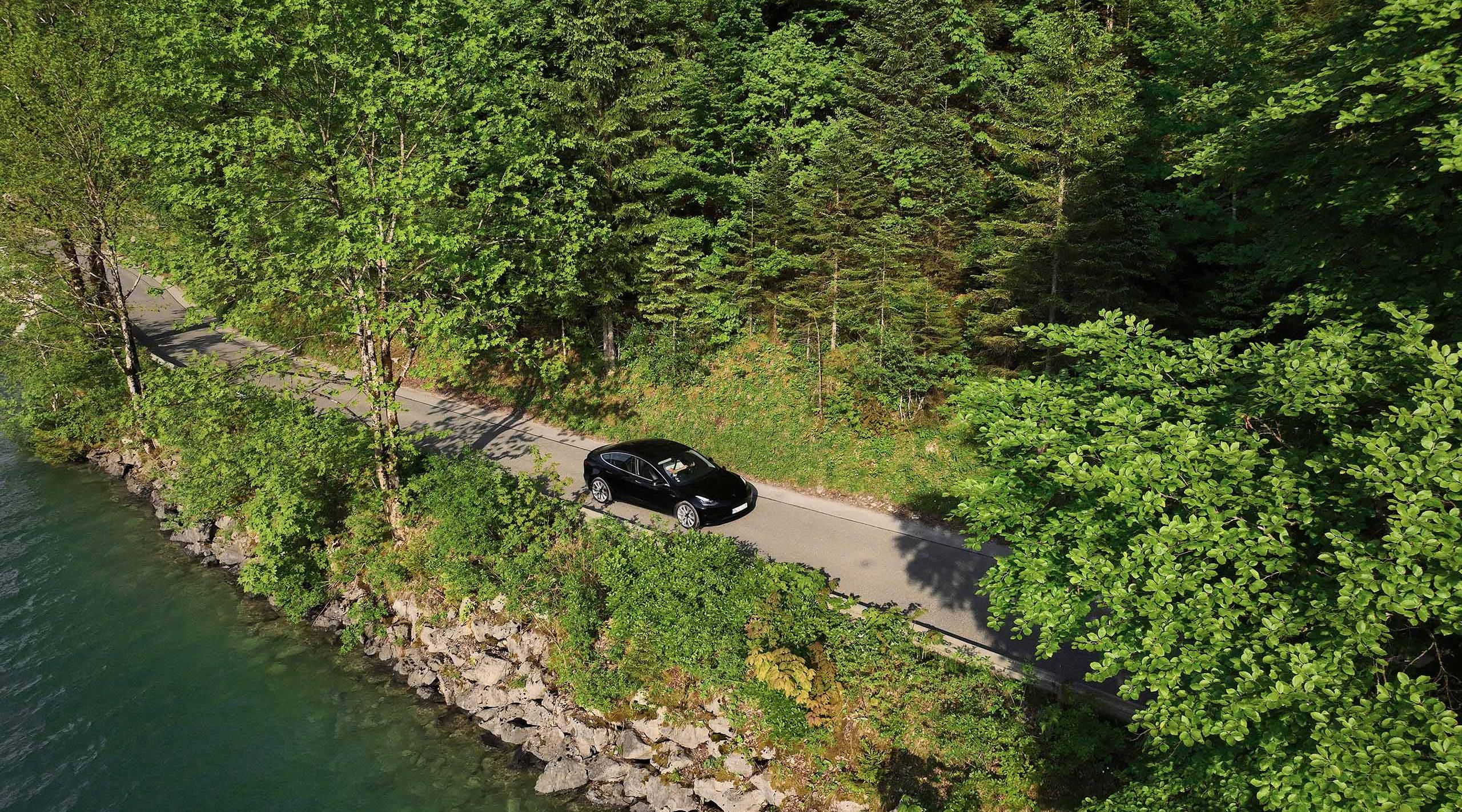 E-Auto faehrt auf einer Straße neben einem See