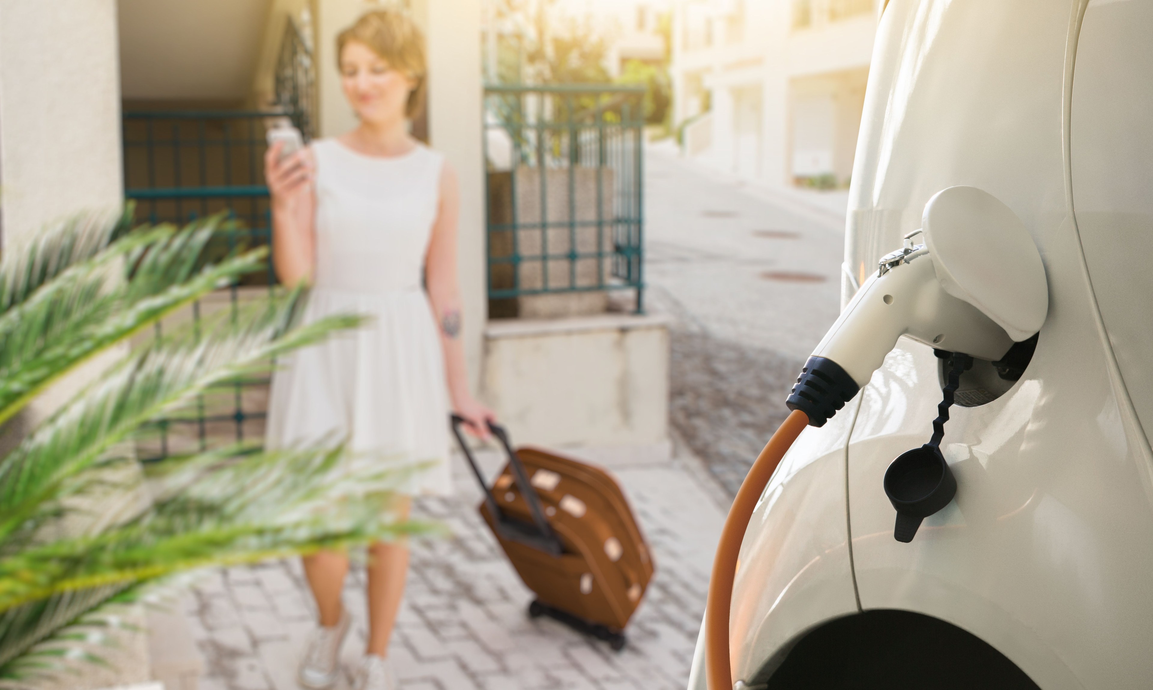 Frau geht mit Koffer zum ladenden E-Auto